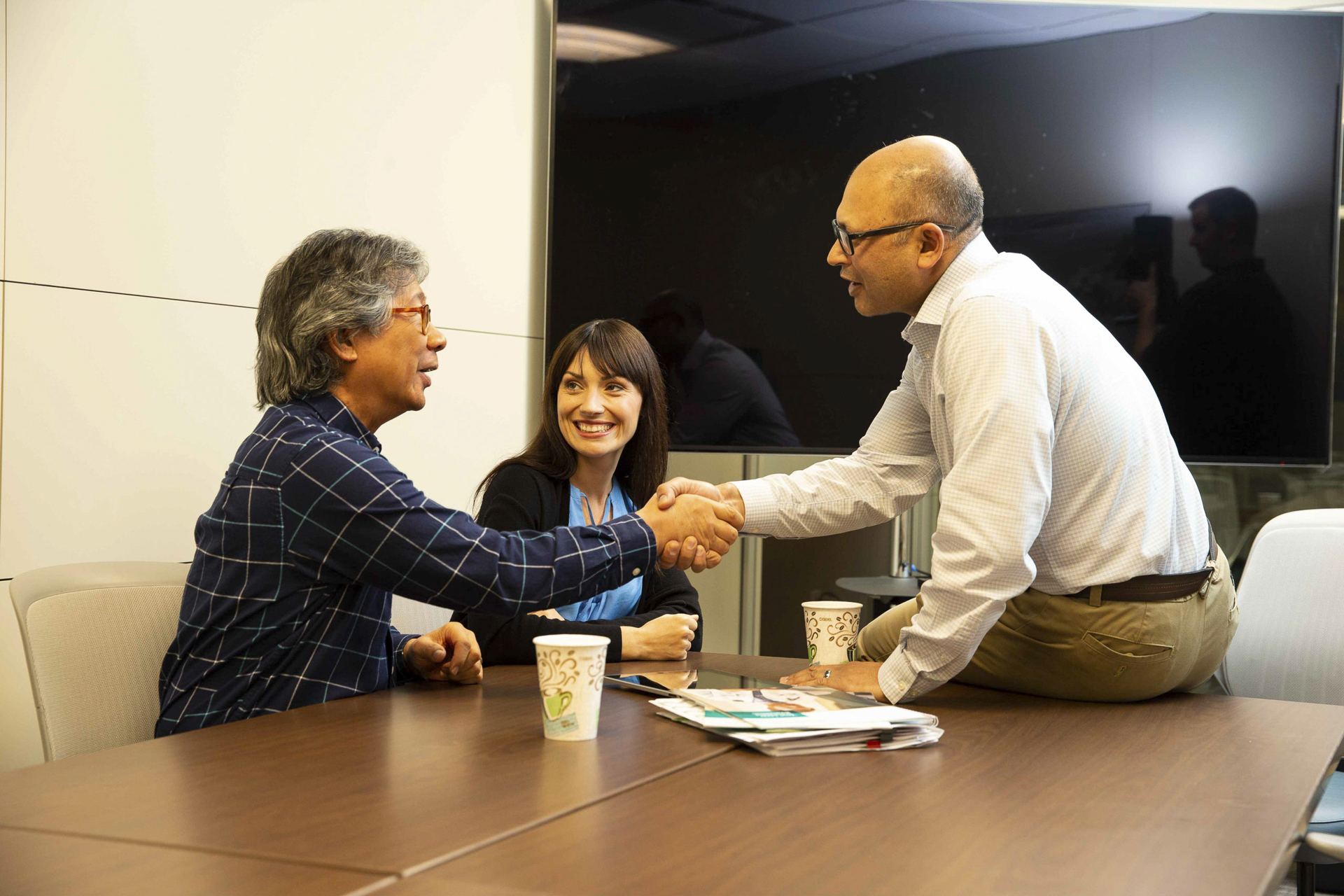 Three people meeting around a conference table, two shaking hands