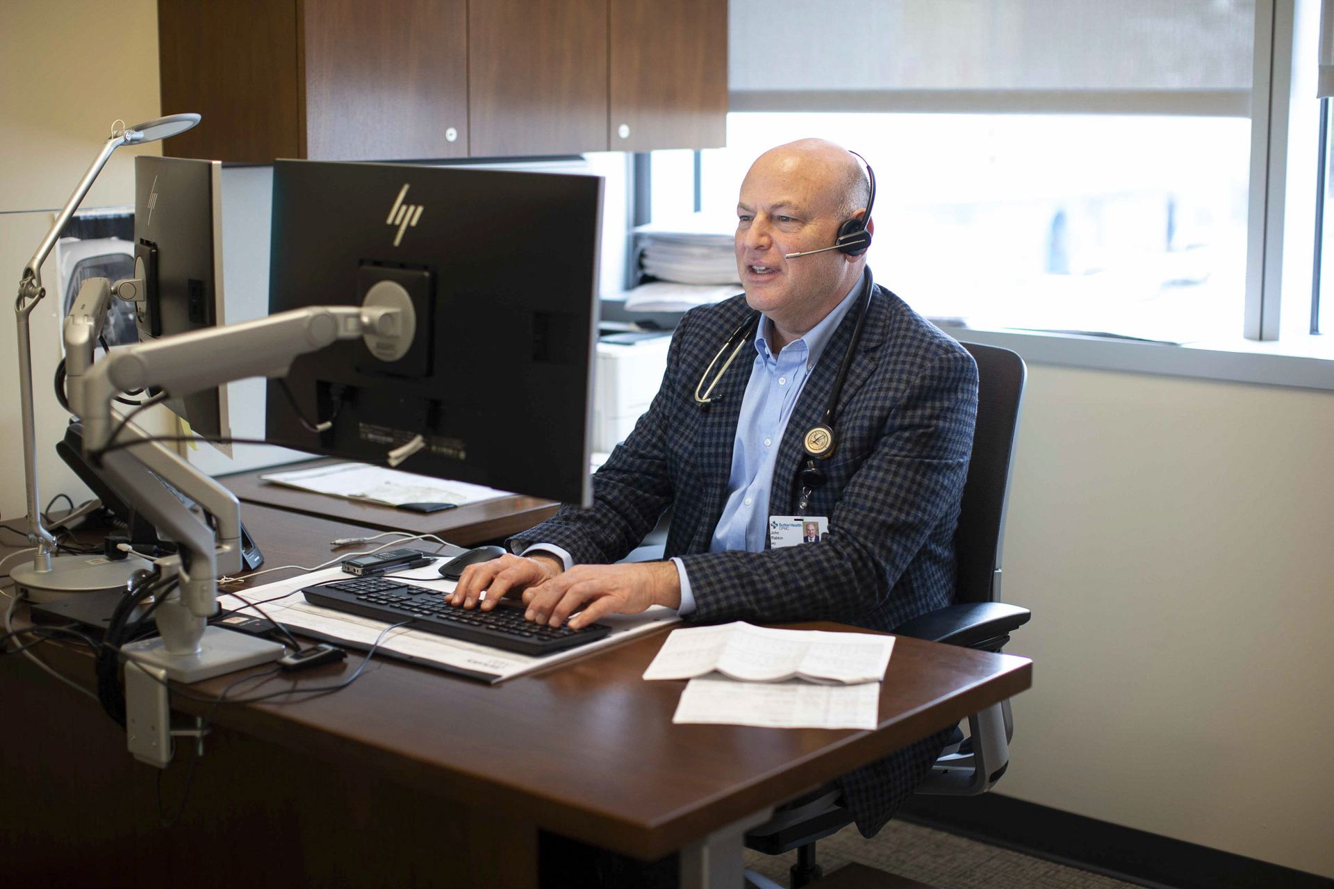 Man at an office desk wearing a headset, working at dual monitors